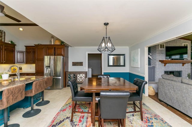 dining area with ceiling fan with notable chandelier, a brick fireplace, ornamental molding, and sink