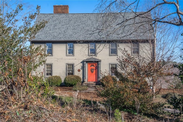 colonial house featuring roof with shingles and a chimney