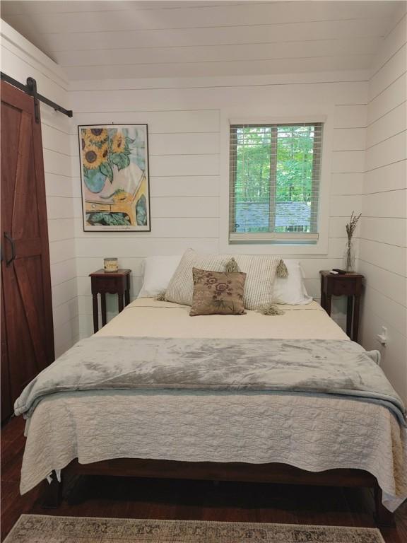 bedroom featuring dark hardwood / wood-style flooring, a barn door, and wooden walls