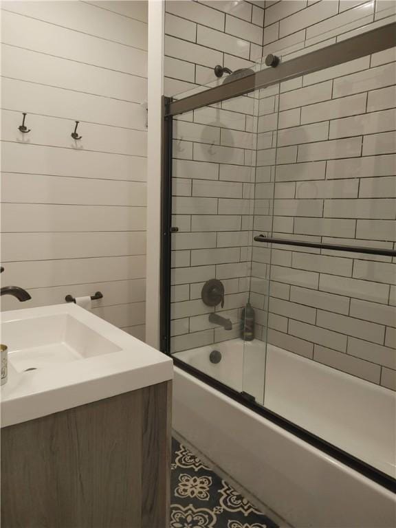 bathroom with wood walls, combined bath / shower with glass door, and sink