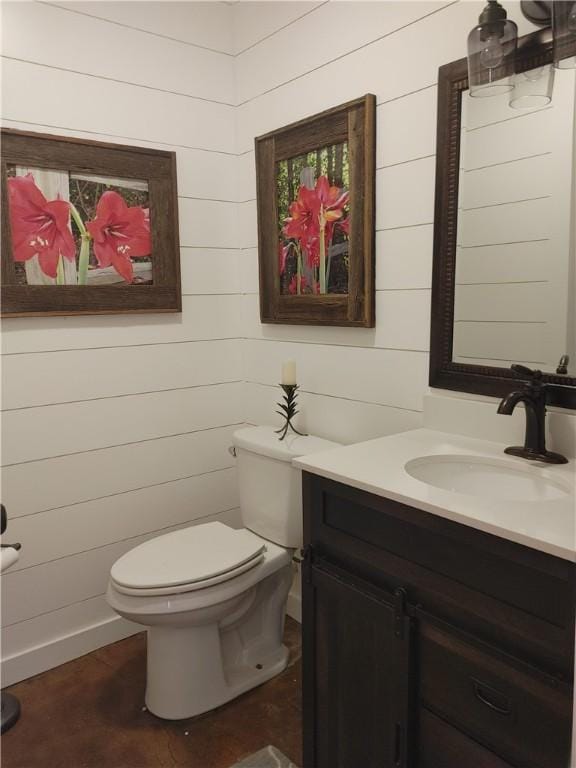 bathroom featuring vanity, toilet, and wooden walls