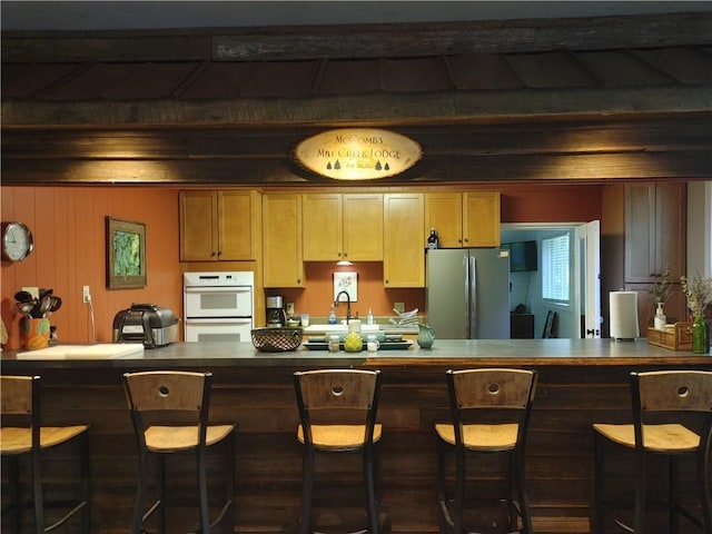 kitchen with a kitchen breakfast bar, stainless steel refrigerator, double oven, and wooden walls