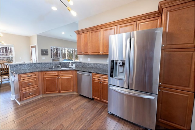 kitchen featuring kitchen peninsula, appliances with stainless steel finishes, dark stone counters, dark wood-type flooring, and sink