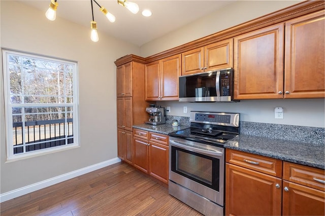 kitchen featuring hardwood / wood-style flooring, dark stone countertops, stainless steel appliances, and hanging light fixtures