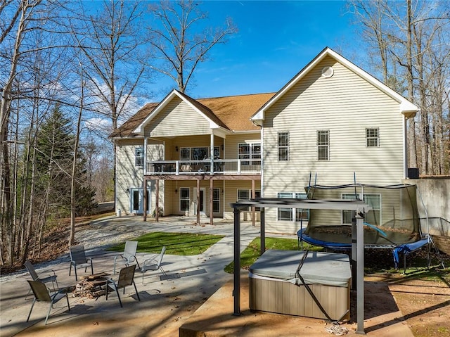 back of property featuring a balcony, a trampoline, a hot tub, and a patio area