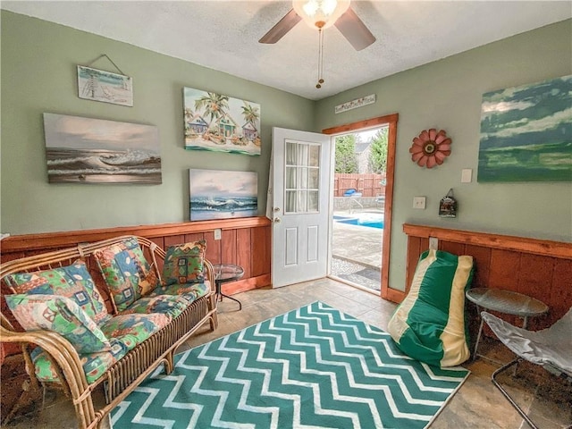 sitting room featuring ceiling fan and wooden walls