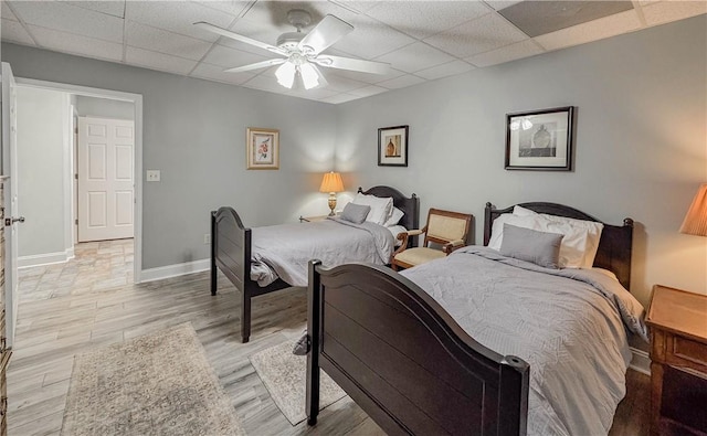 bedroom featuring ceiling fan, a drop ceiling, and light wood-type flooring