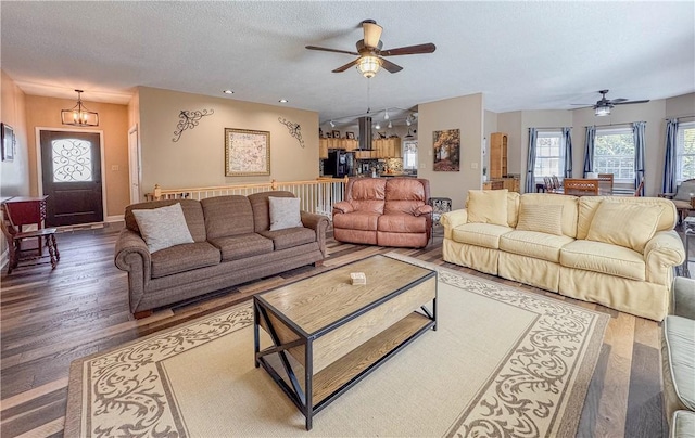 living room with ceiling fan with notable chandelier, wood-type flooring, and a textured ceiling