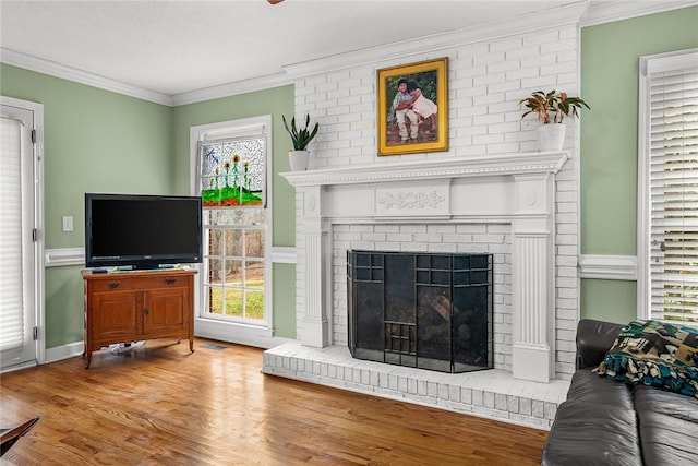 living room featuring a fireplace, a healthy amount of sunlight, light wood-type flooring, and ornamental molding