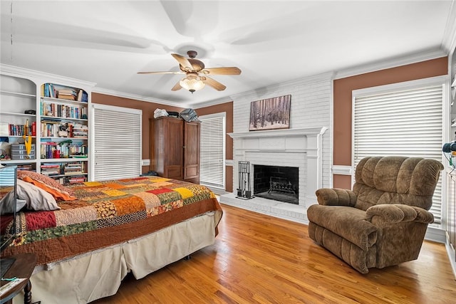 bedroom featuring ceiling fan, crown molding, a fireplace, and light hardwood / wood-style flooring