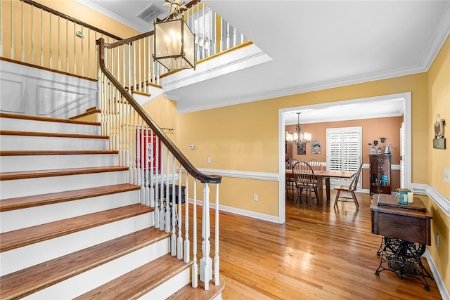 staircase with wood-type flooring, crown molding, and a chandelier