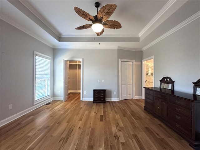 unfurnished bedroom featuring a raised ceiling, ceiling fan, hardwood / wood-style floors, and ornamental molding