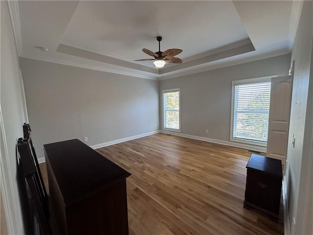 unfurnished room with a raised ceiling, ceiling fan, ornamental molding, and hardwood / wood-style flooring