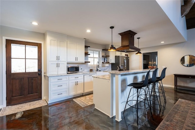 kitchen with appliances with stainless steel finishes, light stone counters, a center island, white cabinetry, and hanging light fixtures