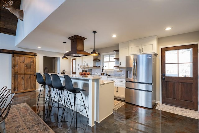 kitchen with stainless steel refrigerator with ice dispenser, light stone counters, a barn door, white cabinetry, and hanging light fixtures