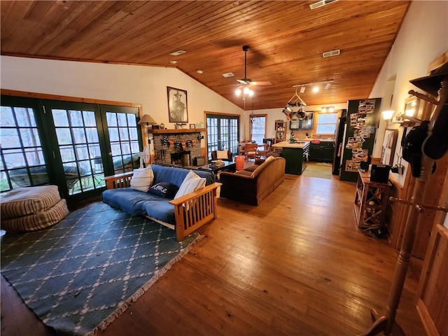 living room featuring wood ceiling, vaulted ceiling, ceiling fan, hardwood / wood-style floors, and a stone fireplace