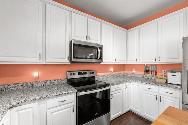 kitchen with white cabinets, light stone counters, stainless steel appliances, and dark wood-type flooring