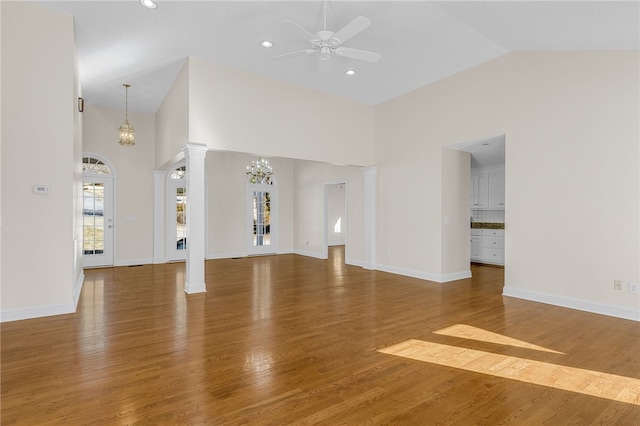 unfurnished living room featuring ceiling fan with notable chandelier, wood-type flooring, and high vaulted ceiling