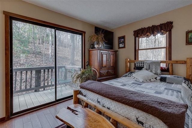 bedroom with access to outside, a textured ceiling, and hardwood / wood-style flooring