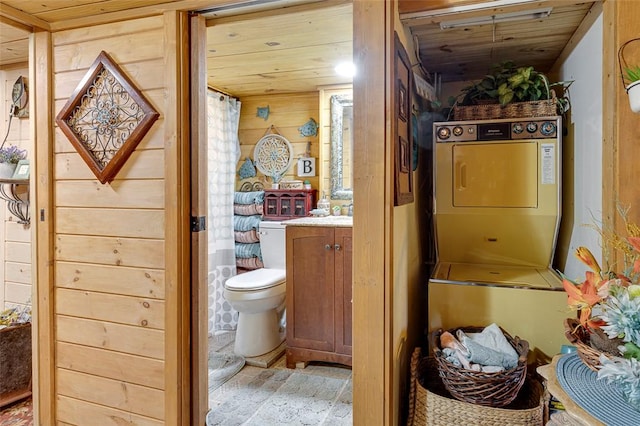 bathroom featuring toilet, wood ceiling, stacked washer and clothes dryer, wooden walls, and vanity