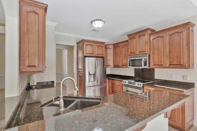 kitchen with appliances with stainless steel finishes, ornamental molding, dark stone countertops, and sink