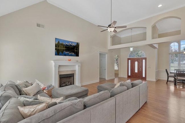 living room with ceiling fan, ornamental molding, a high ceiling, and light hardwood / wood-style flooring