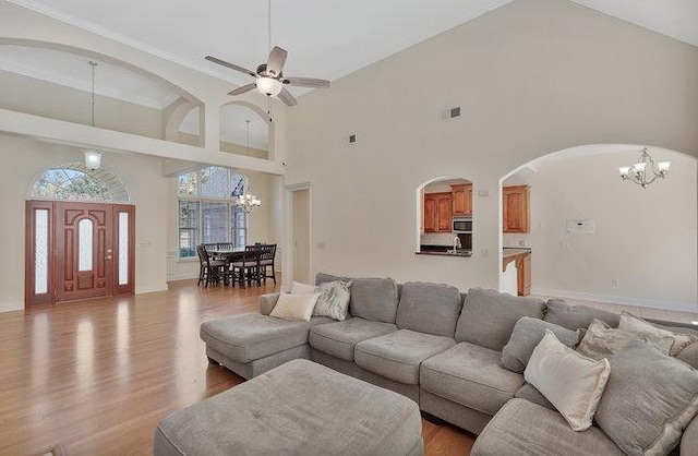 living room featuring a high ceiling, ceiling fan with notable chandelier, and light wood-type flooring