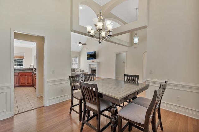 dining space with a healthy amount of sunlight, high vaulted ceiling, light hardwood / wood-style floors, and ceiling fan with notable chandelier