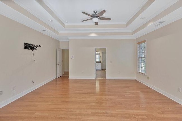 empty room featuring ceiling fan, a raised ceiling, light wood-type flooring, and crown molding