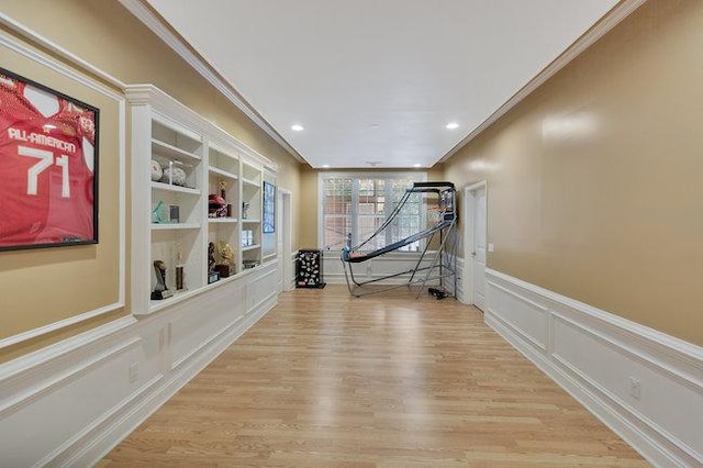 workout room with built in shelves, crown molding, and light wood-type flooring