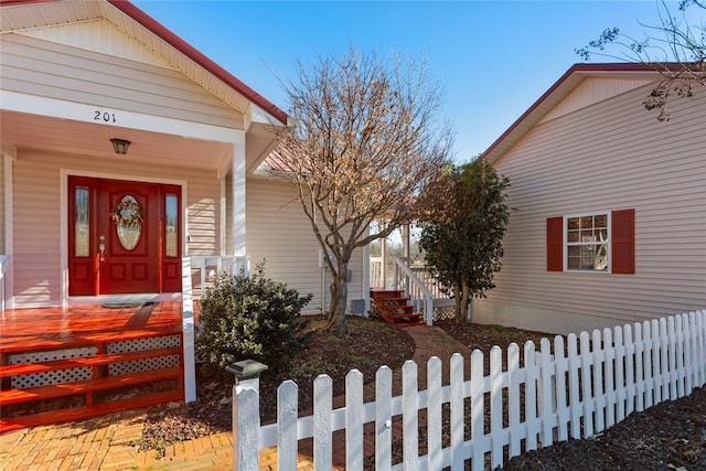 view of exterior entry with covered porch and fence