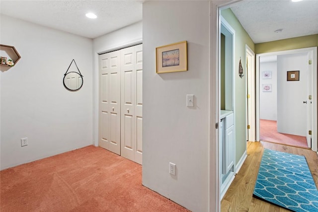 hall with a textured ceiling and light colored carpet