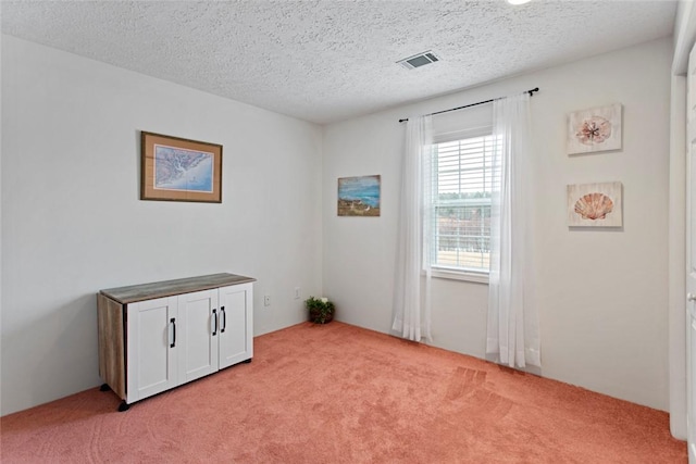 spare room with light carpet, visible vents, and a textured ceiling