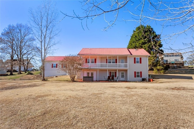 rear view of house with metal roof, a yard, and a balcony