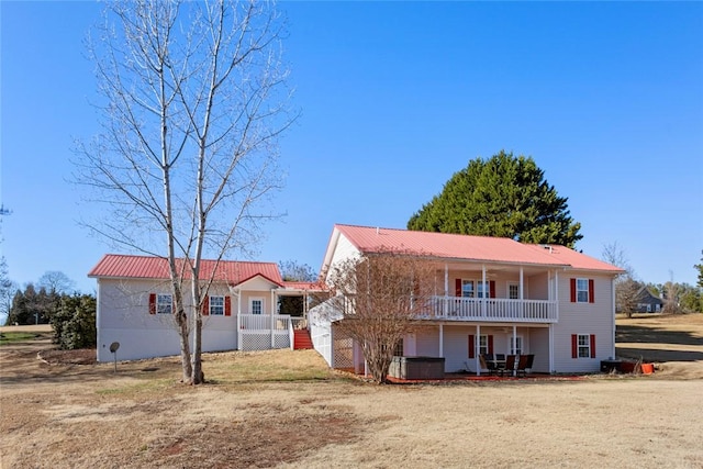 back of house featuring covered porch, metal roof, and a balcony