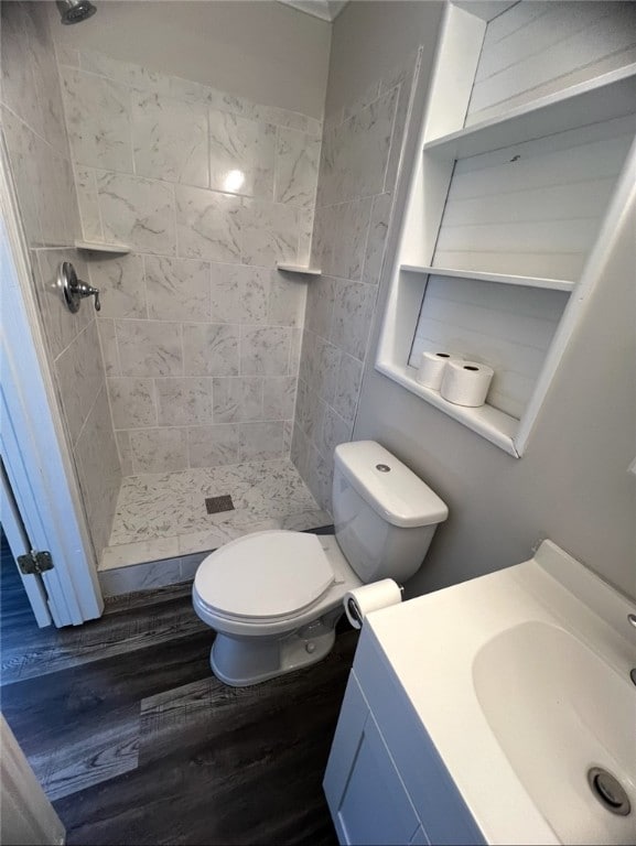 bathroom with a tile shower, vanity, toilet, and hardwood / wood-style floors