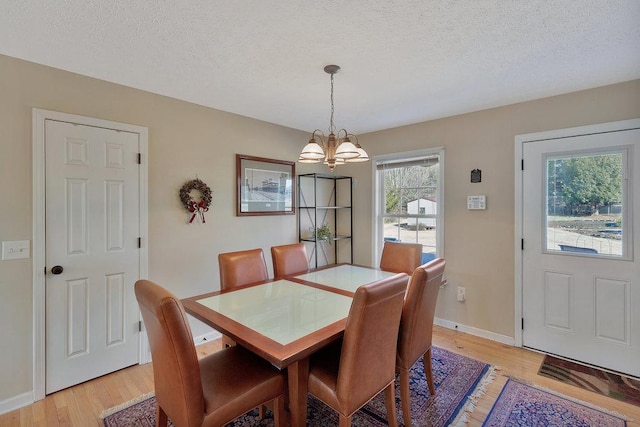 dining space with a notable chandelier, light wood-type flooring, and a textured ceiling