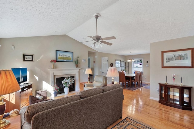 living room with baseboards, a premium fireplace, lofted ceiling, light wood-style floors, and ceiling fan with notable chandelier