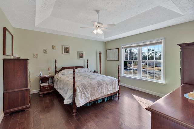 bedroom featuring baseboards, a textured ceiling, a tray ceiling, and wood-type flooring