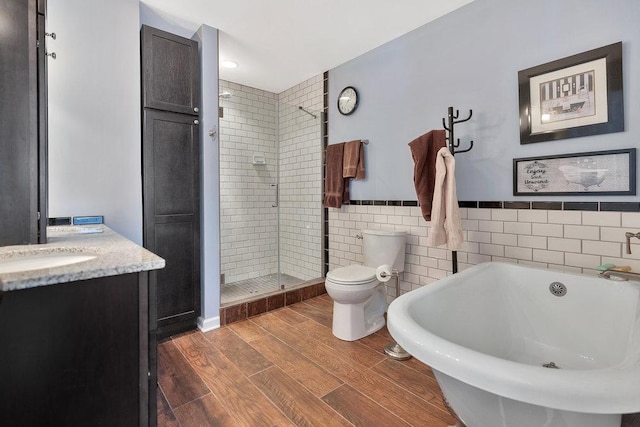 bathroom featuring wood finished floors, a freestanding bath, a shower stall, tile walls, and toilet