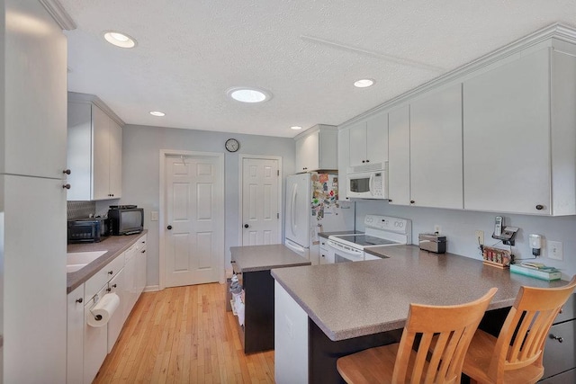 kitchen with white appliances, a breakfast bar area, a peninsula, light wood-style flooring, and a textured ceiling