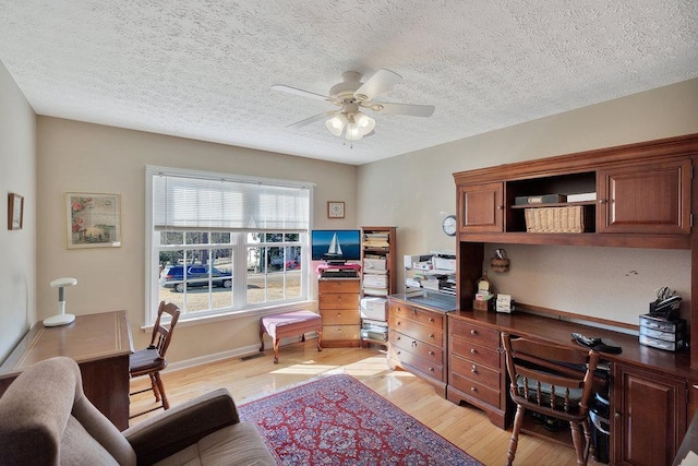 home office featuring a ceiling fan, light wood-style floors, baseboards, and a textured ceiling