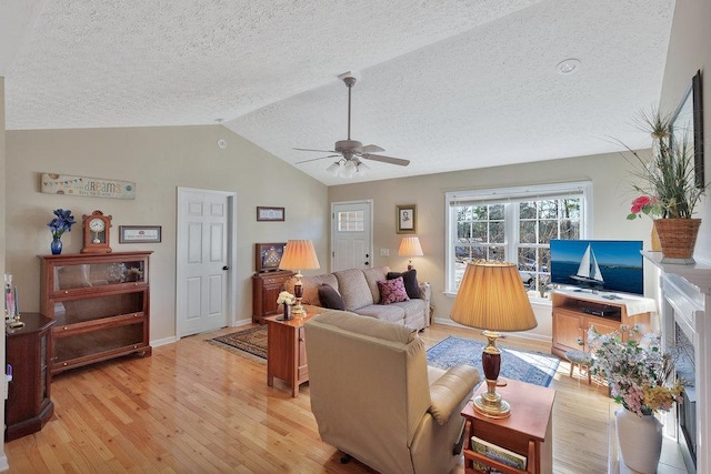 living room featuring a ceiling fan, baseboards, lofted ceiling, light wood-style flooring, and a textured ceiling