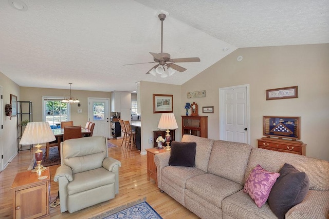 living room with ceiling fan with notable chandelier, light wood-style flooring, a textured ceiling, and lofted ceiling