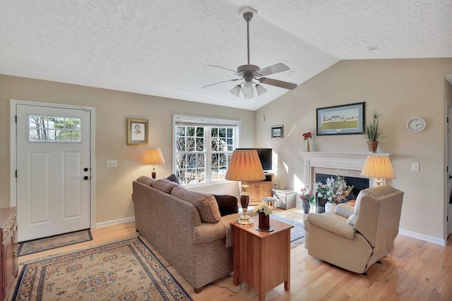 living area featuring ceiling fan, vaulted ceiling, light wood-style flooring, and a tile fireplace