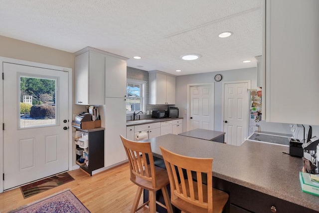 kitchen with a breakfast bar area, a peninsula, a sink, light wood-style floors, and a textured ceiling