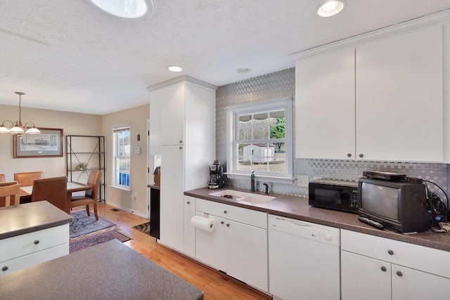 kitchen featuring dark countertops, black microwave, light wood-style flooring, white dishwasher, and a sink