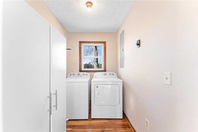 laundry area featuring a textured ceiling, electric panel, light hardwood / wood-style flooring, and washing machine and clothes dryer