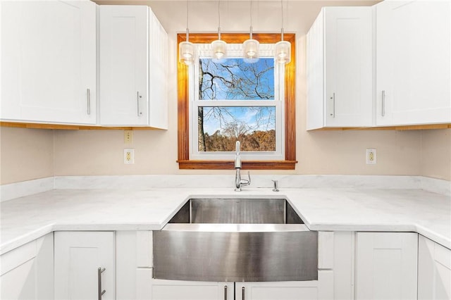 kitchen with white cabinetry, sink, hanging light fixtures, and light stone counters