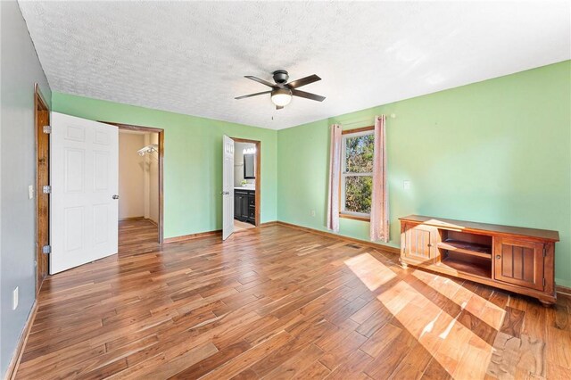 unfurnished bedroom featuring a walk in closet, ensuite bath, a textured ceiling, ceiling fan, and hardwood / wood-style flooring